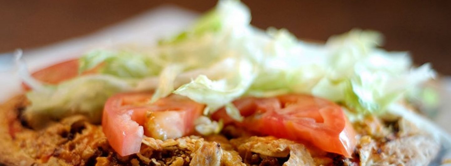 taco pizza with ground beef, tortilla chips, tomatoes and lettuce ontop